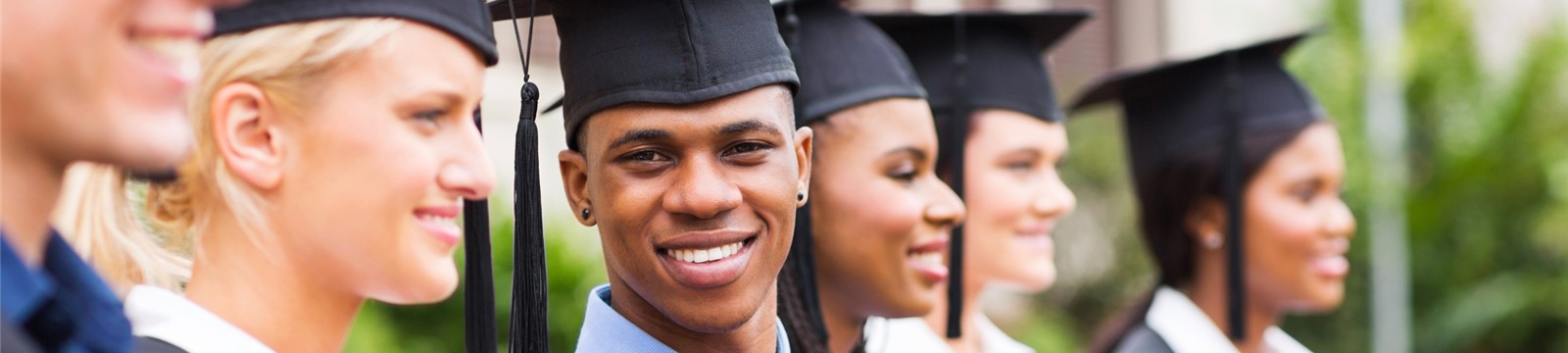 Smiling high school graduates in caps and gowns pose for pictures. Handsome young man looks directly at camera.