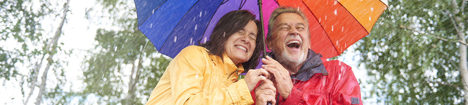 image of couple laughing under colorful umbrella in rain storm